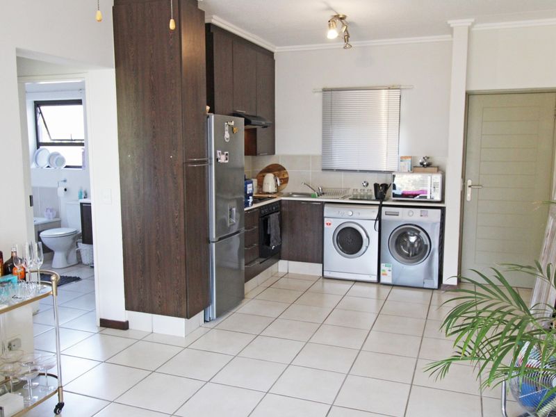 Compact kitchen featuring dark wood cabinetry, tiled flooring, built-in oven, and integrated laundry appliance space, with an adjacent view into the bathroom.