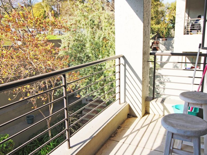A covered balcony featuring a metal balustrade and tiled flooring, overlooking a garden area.