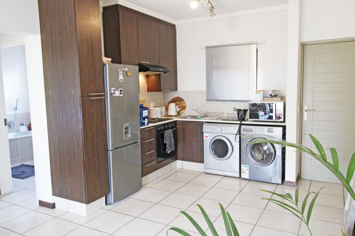 A functional kitchen featuring dark wood cabinetry, tiled flooring, built-in oven and hob, and integrated laundry appliance connections.
