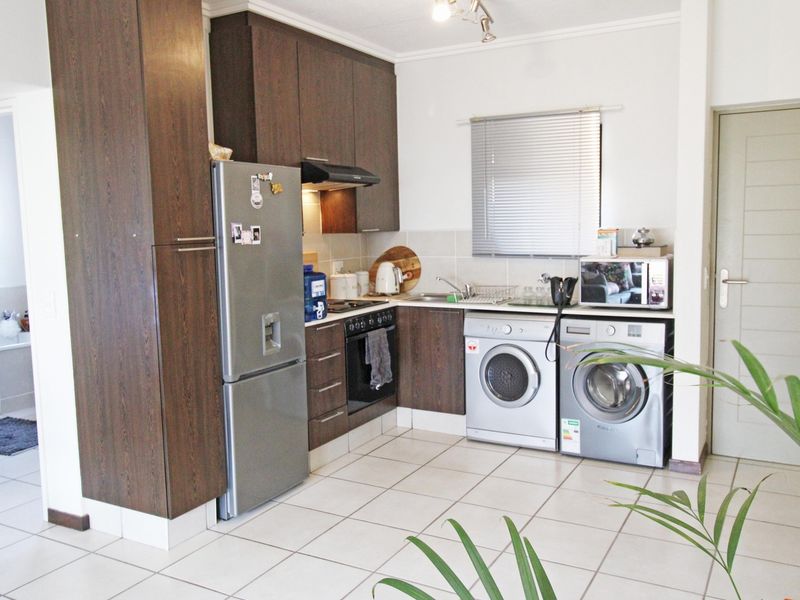 A functional kitchen featuring dark wood cabinetry, tiled flooring, built-in oven and hob, and integrated laundry appliance connections.