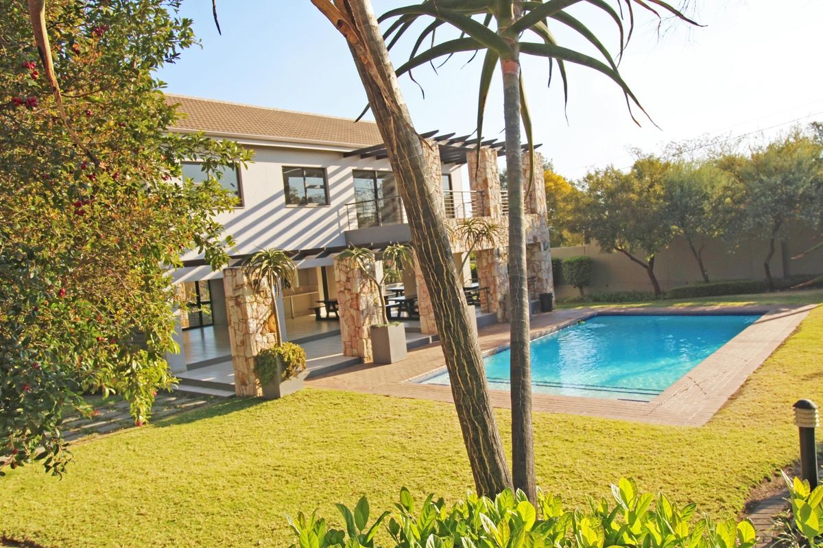 Rear view of the property featuring a swimming pool, landscaped garden, and a covered patio area with stone-clad pillars.
