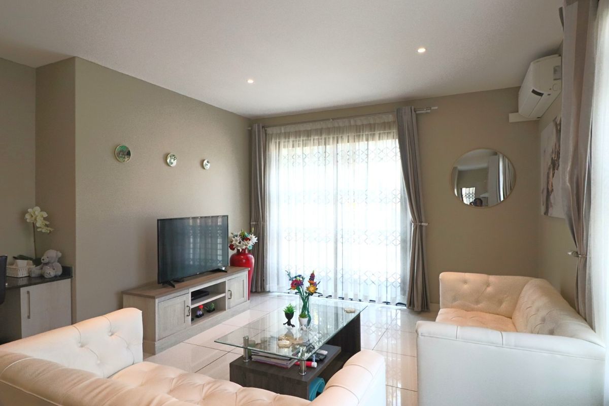 A well-maintained living room featuring tiled flooring, recessed downlighting, and a split-system air conditioner, with direct access to an outdoor area via sliding doors.