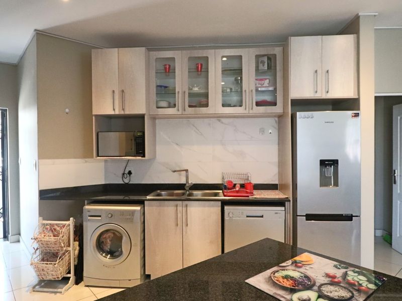 A functional kitchen featuring light wood cabinetry, dark stone countertops, marble-look splashback, and integrated space for laundry and dishwashing appliances.