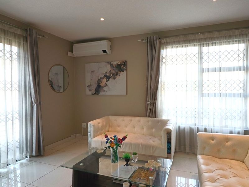A bright and well-maintained living room featuring tiled flooring, recessed downlighting, and a wall-mounted split-system air conditioner for climate control.