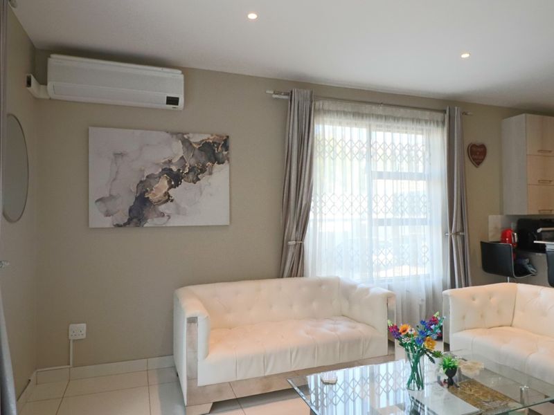 An open-plan living area featuring tiled flooring, recessed lighting, and a wall-mounted air conditioning unit, seamlessly connected to a functional kitchen space.