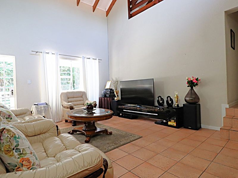 Spacious living room featuring high vaulted ceilings with exposed timber beams and terracotta floor tiles, offering a bright and airy atmosphere.