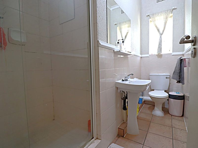 A functional bathroom featuring a pedestal sink, toilet, and a glass-enclosed shower with neutral wall and floor tiling.