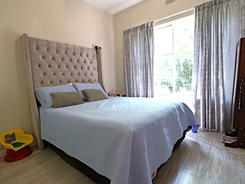 A bedroom featuring laminate flooring and a large sliding glass door with curtains providing natural light.