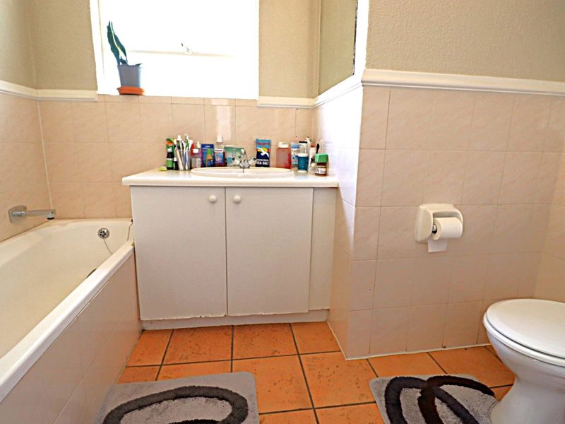 A functional bathroom featuring a bathtub, vanity cabinet with basin, and toilet, finished with neutral wall tiles and terracotta-style floor tiles.