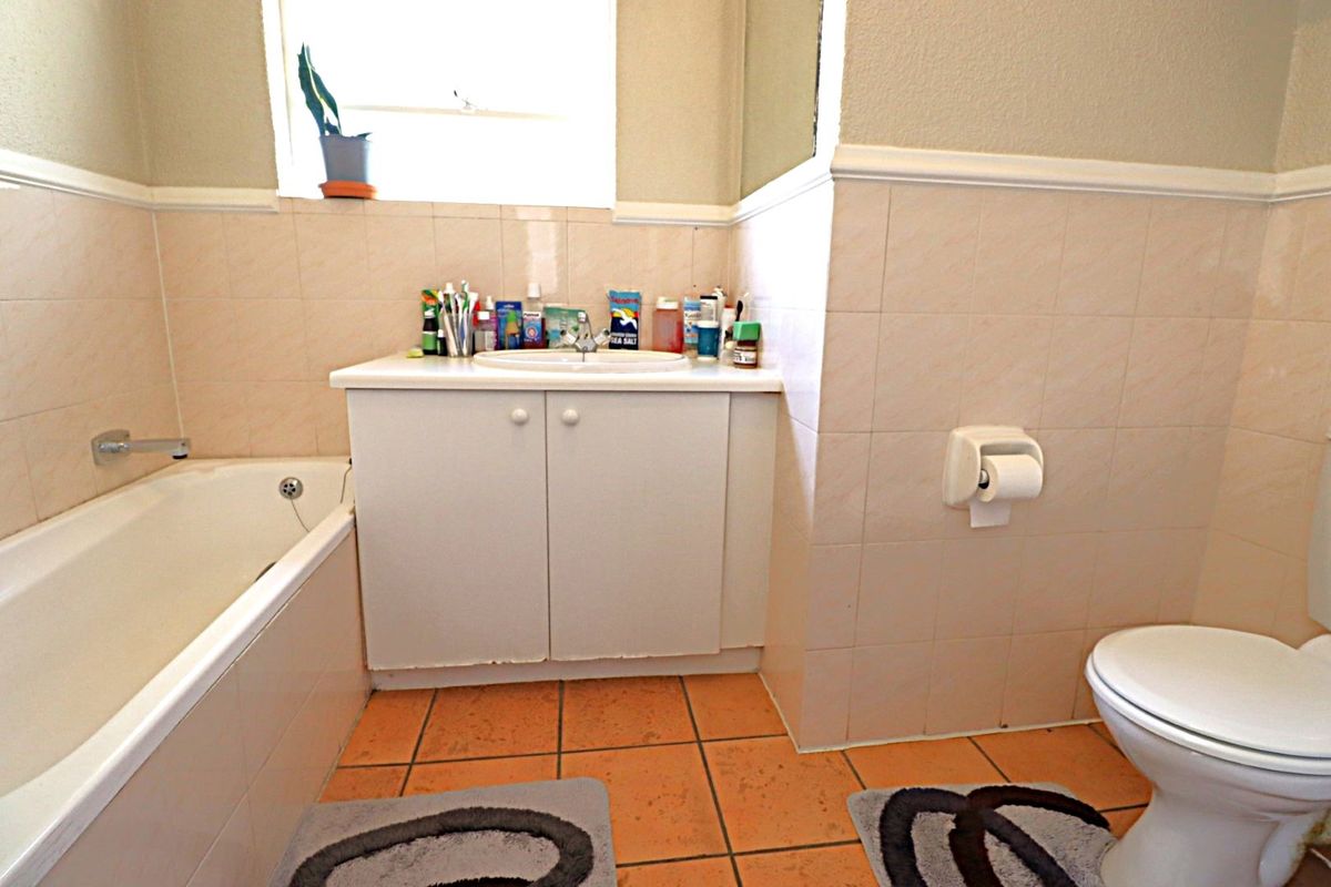 A functional bathroom featuring a bathtub, vanity cabinet with basin, and toilet, finished with neutral wall tiles and terracotta-style floor tiles.