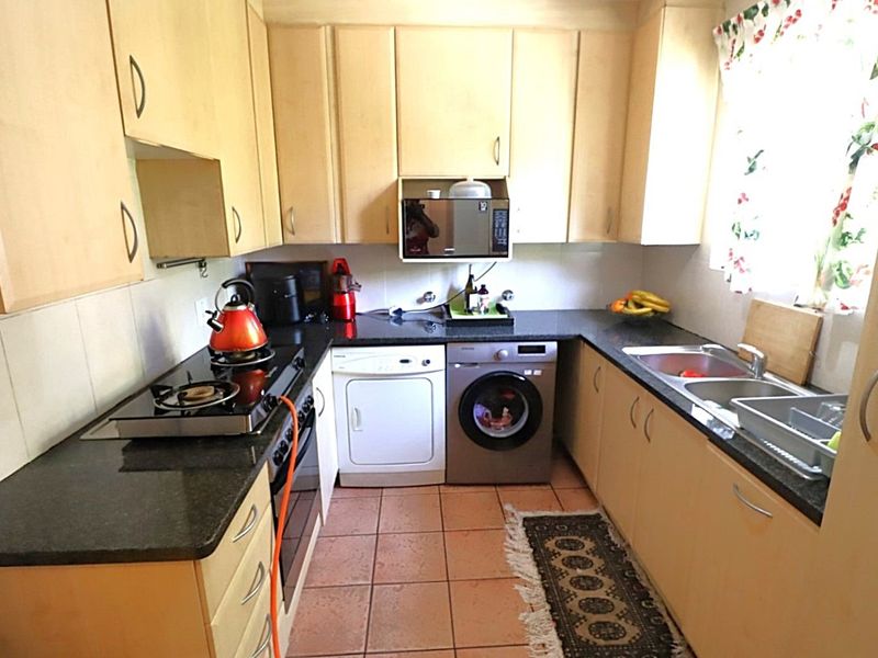 Functional kitchen featuring light wood cabinetry, granite countertops, gas hob, built-in oven, and tiled flooring with space for under-counter appliances.
