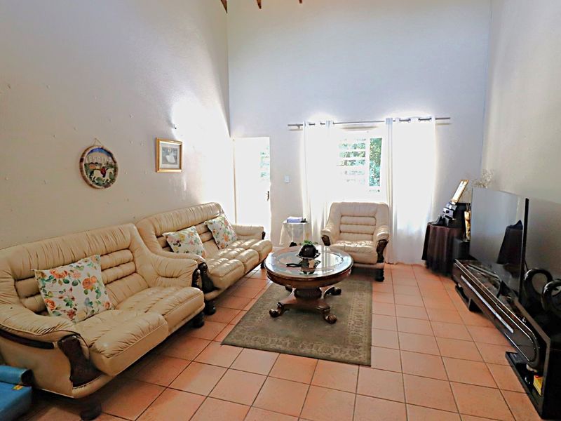 Spacious living room featuring high vaulted ceilings, tiled flooring, and natural light from a large window and door.