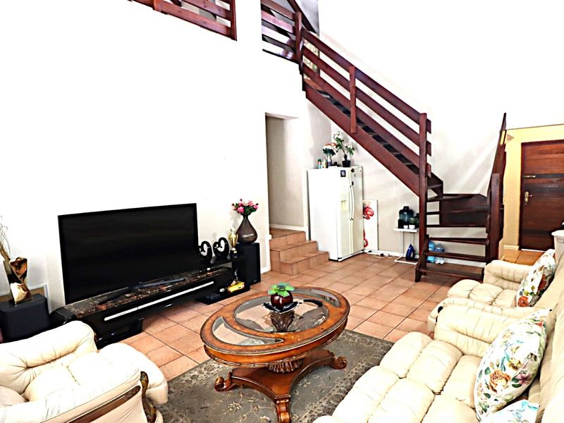 Spacious living room featuring tiled flooring, a prominent wooden staircase leading to an upper level, and high ceilings.