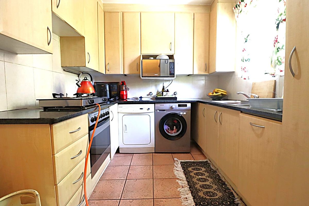 A functional kitchen featuring light wood cabinetry, laminate countertops, a built-in oven with gas hob, and tiled flooring.