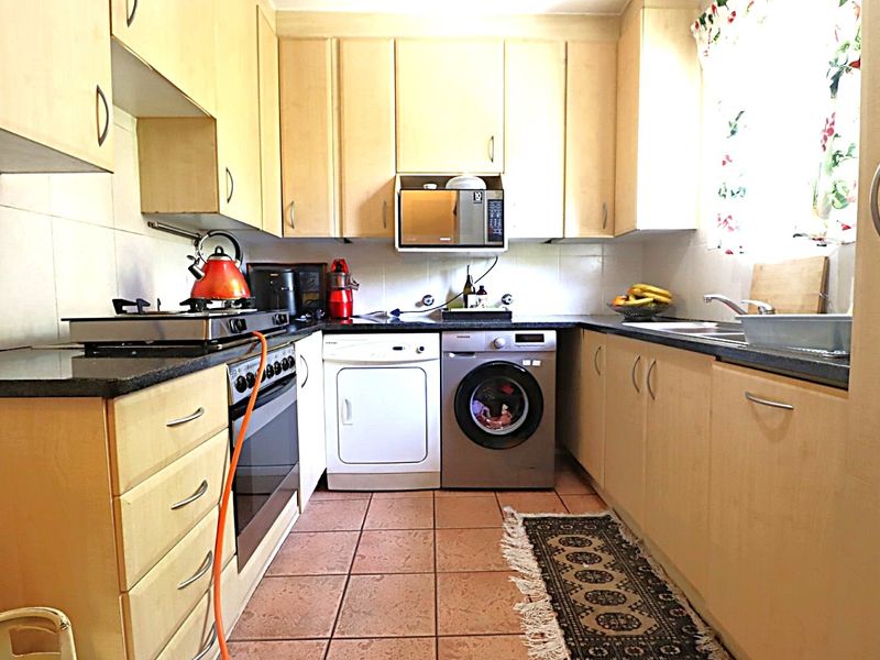 A functional kitchen featuring light wood cabinetry, laminate countertops, a built-in oven with gas hob, and tiled flooring.