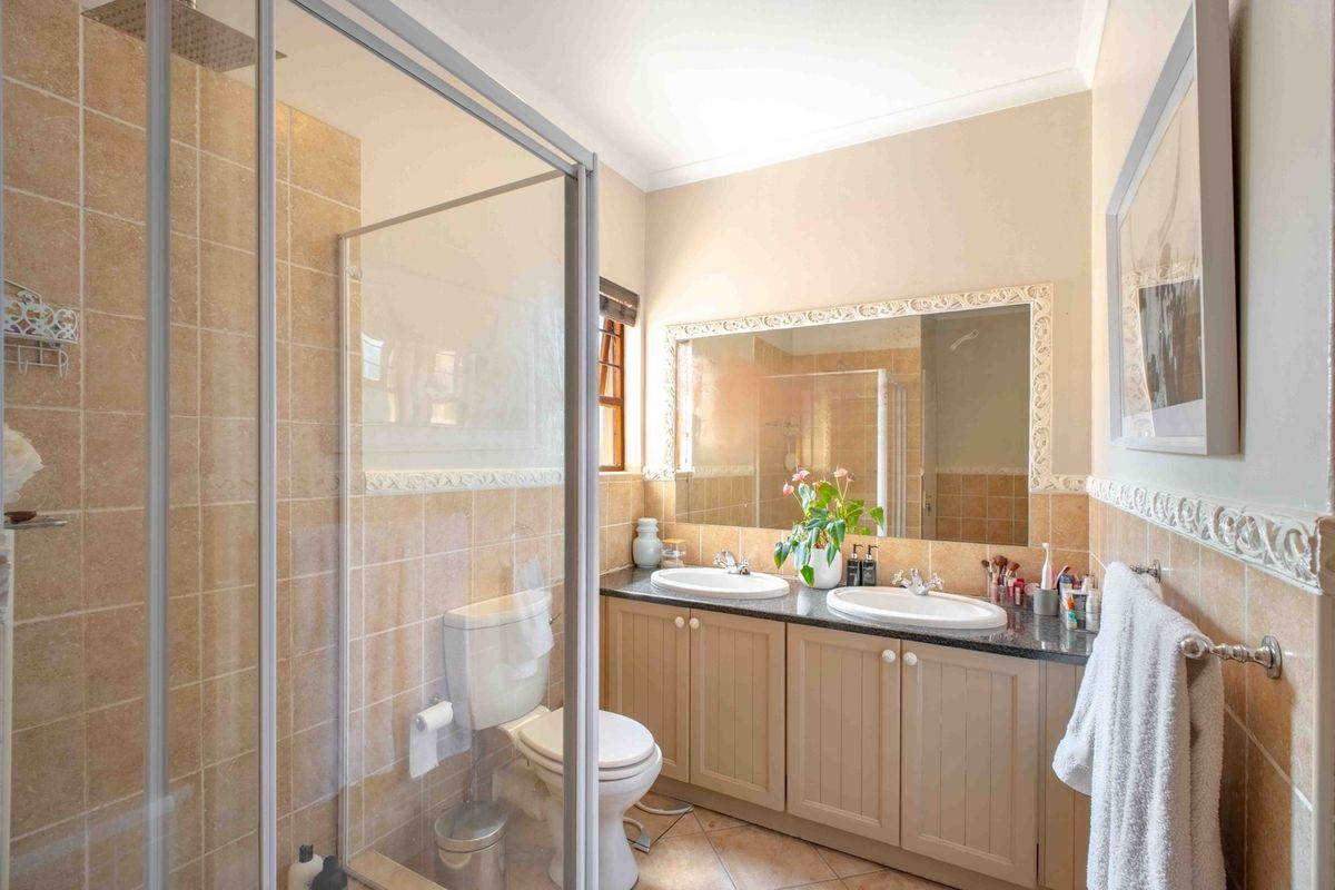 A functional bathroom featuring a double vanity with granite countertops, a glass-enclosed shower, and neutral ceramic tiling throughout.