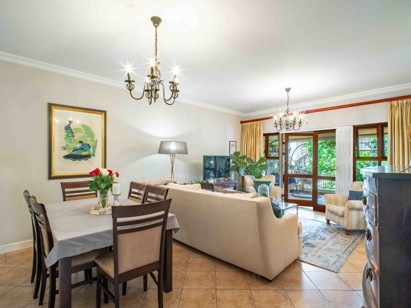 Spacious open-plan living and dining area featuring tiled flooring, elegant chandeliers, and large sliding glass doors leading to an outdoor patio space.