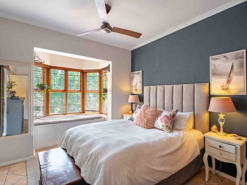 A well-maintained bedroom featuring a large bay window with a built-in window seat, tiled flooring, and a ceiling fan.