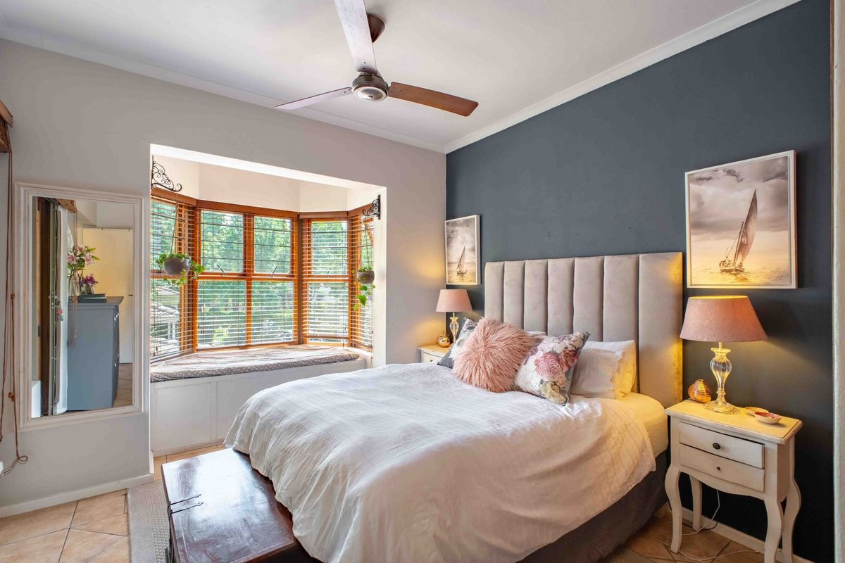 A well-maintained bedroom featuring a large bay window with a built-in window seat, tiled flooring, and a ceiling fan.