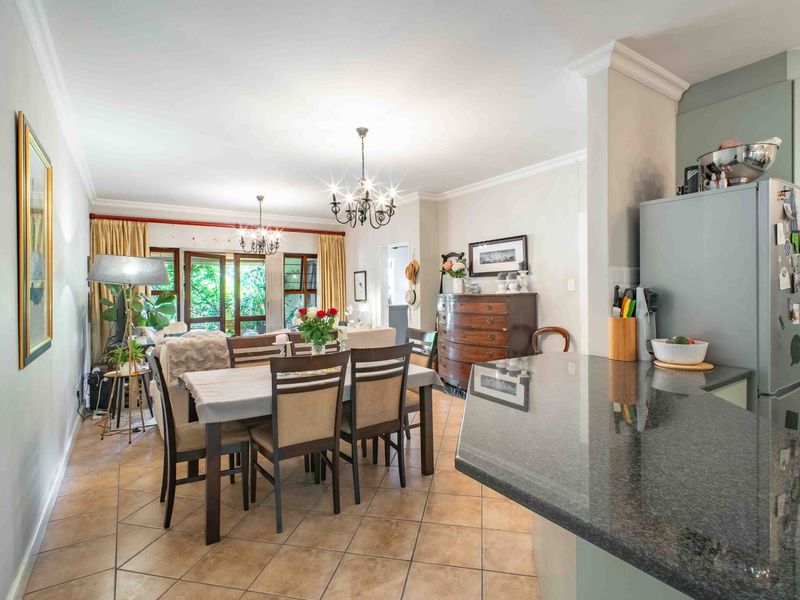 Open-plan living and dining area featuring tiled flooring, crown molding, and a granite kitchen countertop, leading to a bright outdoor patio space.