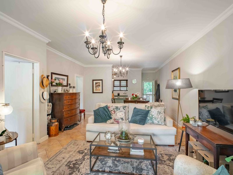 An open-plan living and dining area featuring ceramic tile flooring, crown molding, and a classic wrought iron chandelier, leading to a functional kitchen space.