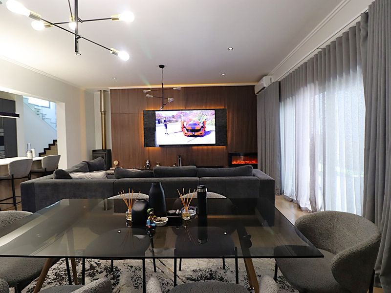 Spacious open-plan living and dining area featuring a wood-panelled feature wall with integrated fireplace, modern lighting, and seamless flow to the kitchen.
