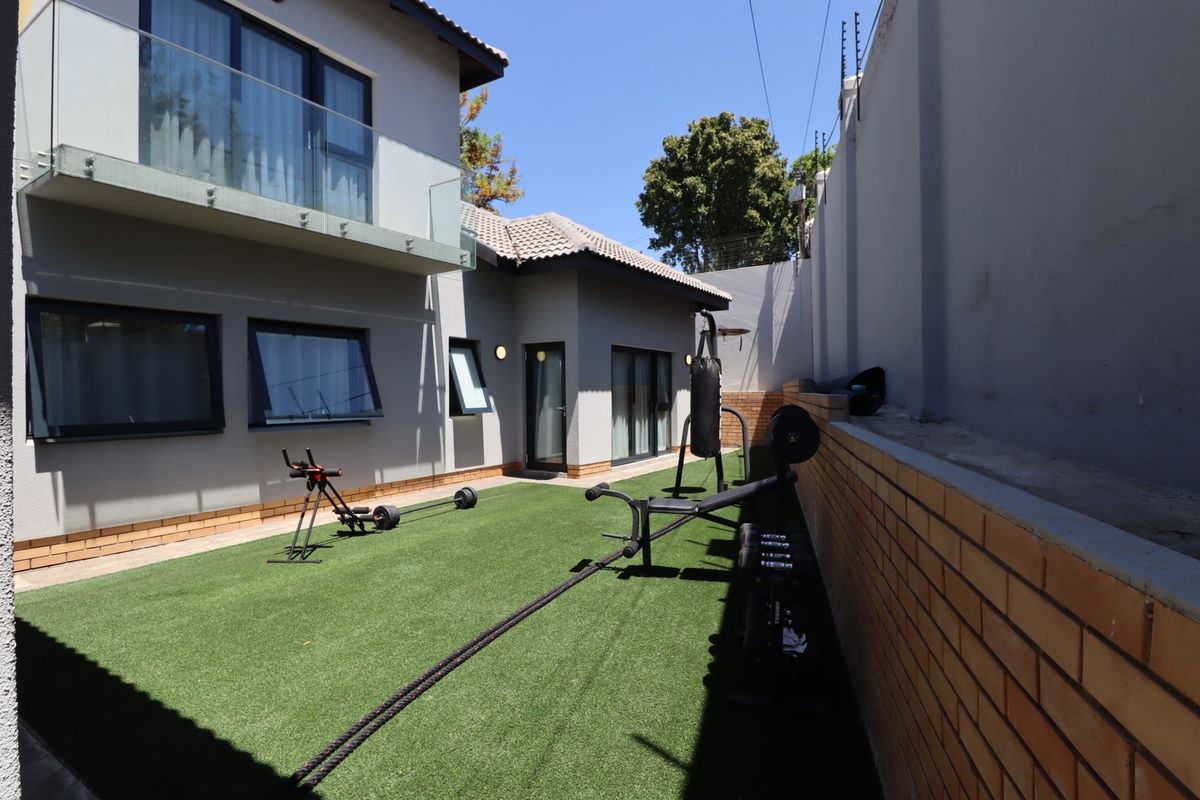 Rear courtyard area featuring artificial turf, a glass-balustraded balcony above, and secure brick boundary walls with electric fencing.