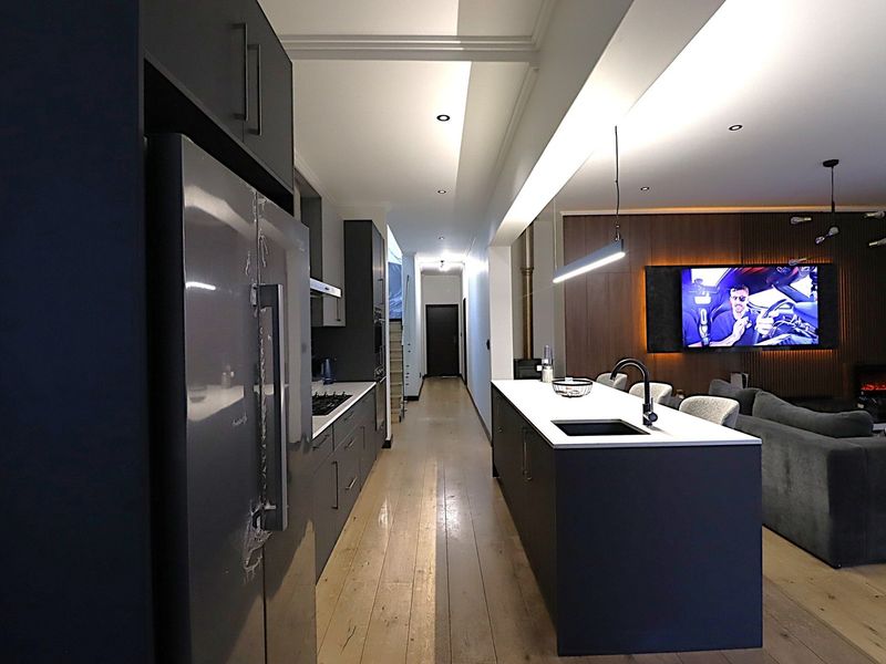 Modern open-plan living area featuring a sleek kitchen with a central island, dark cabinetry, and hardwood flooring, seamlessly flowing into the lounge space.