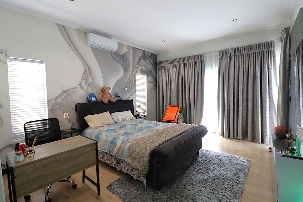A well-maintained bedroom featuring timber flooring, recessed downlighting, a wall-mounted split-system air conditioner, and large windows with integrated curtain tracks and venetian blinds.