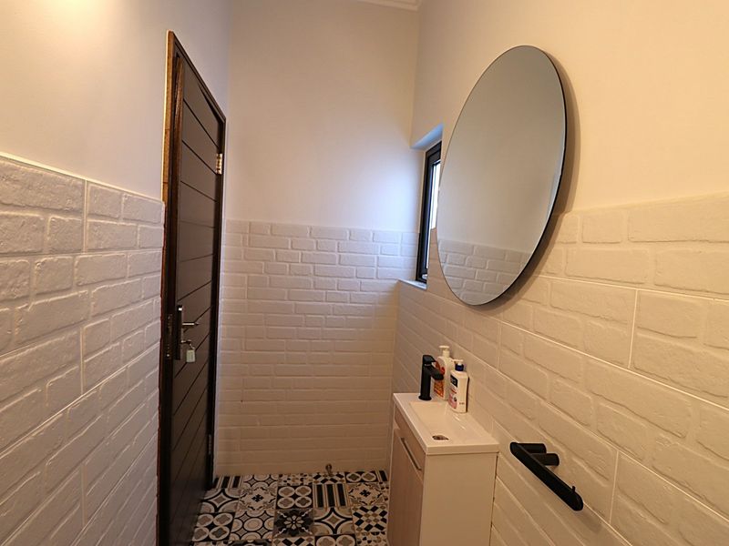 A modern bathroom featuring patterned floor tiles, white brick-effect wall tiling, a vanity basin, and a circular wall-mounted mirror.