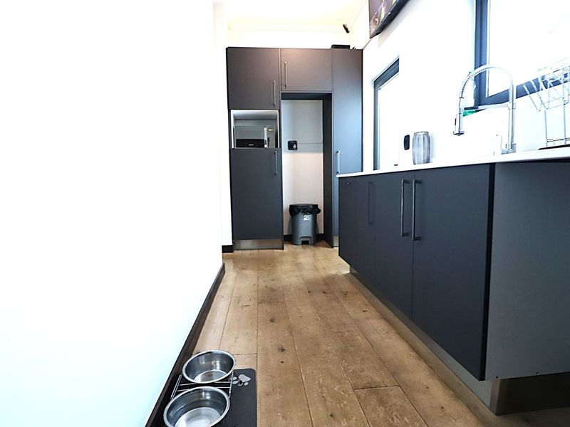 Modern laundry room featuring dark matte cabinetry, a stainless steel sink with a gooseneck faucet, and durable hardwood flooring.