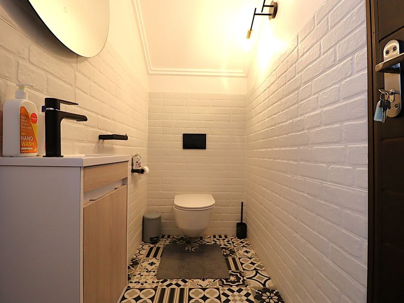 Modern guest bathroom featuring a wall-mounted toilet, vanity cabinet with basin, and decorative patterned floor tiles.