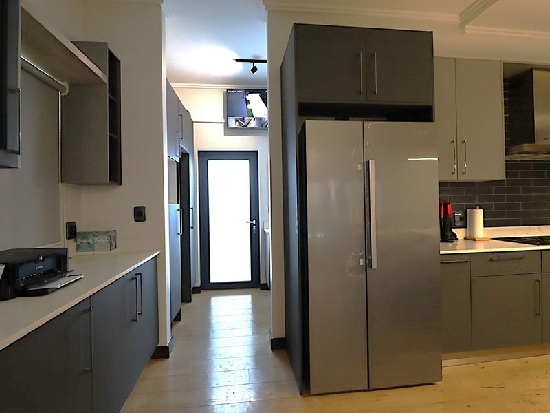Modern kitchen featuring sleek grey cabinetry, stone countertops, a tiled backsplash, and integrated appliances, leading to a rear exterior door.