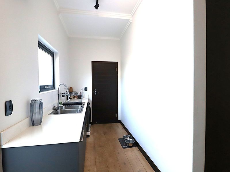 A clean and functional scullery featuring modern cabinetry, a stainless steel sink, and timber flooring, providing additional prep and wash-up space.