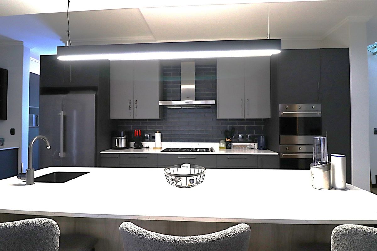 Modern kitchen featuring a large central island, dark cabinetry, subway tile backsplash, integrated appliances, and sleek pendant lighting.