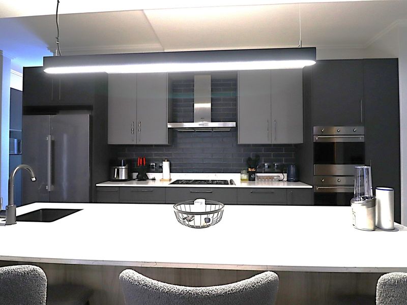 Modern kitchen featuring a large central island, dark cabinetry, subway tile backsplash, integrated appliances, and sleek pendant lighting.