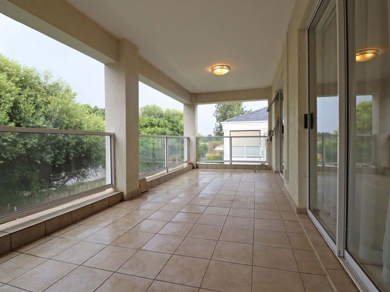 A spacious covered balcony featuring tiled flooring, a modern glass balustrade, and large sliding glass doors providing access to the interior living space.