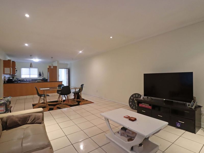 Spacious open-plan living and dining area featuring tiled flooring, recessed lighting, and a functional kitchen with built-in cabinetry and a breakfast counter.