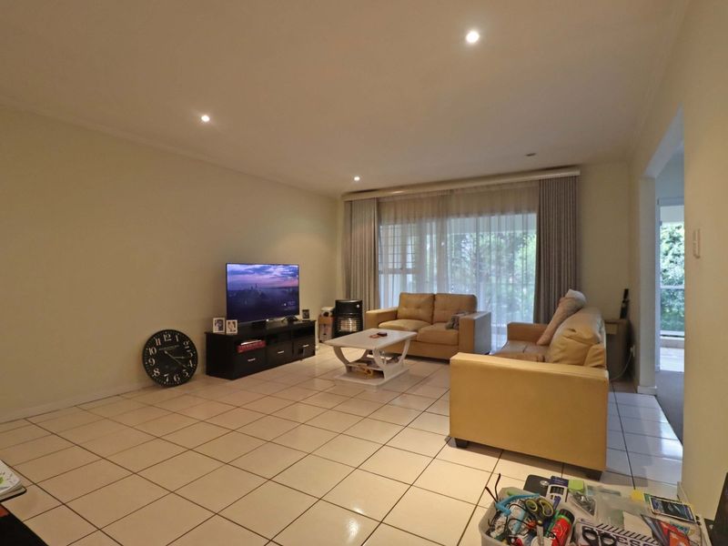 Spacious living room featuring neutral ceramic floor tiles, recessed downlighting, and large sliding glass doors providing access to the outdoor area.