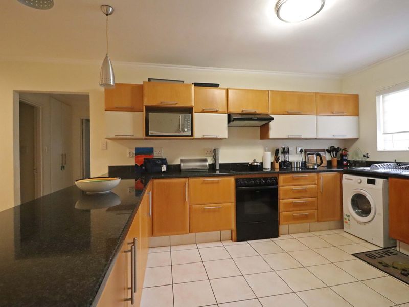 Functional kitchen featuring granite countertops, wooden cabinetry, built-in microwave, extractor fan, and tiled flooring with space for a washing machine.