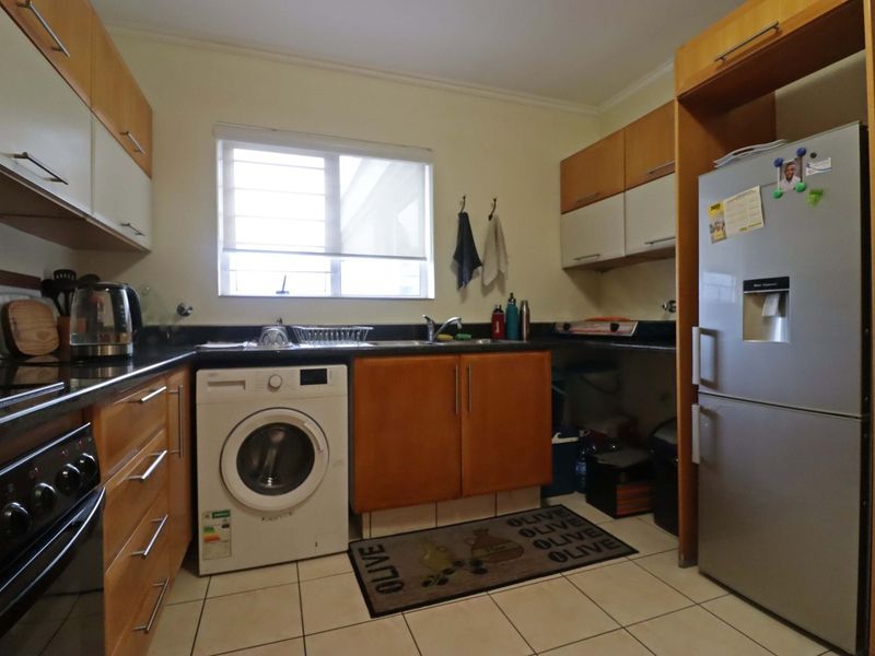 Functional kitchen featuring wooden cabinetry, granite countertops, built-in oven, hob, and tiled flooring with space for a washing machine.