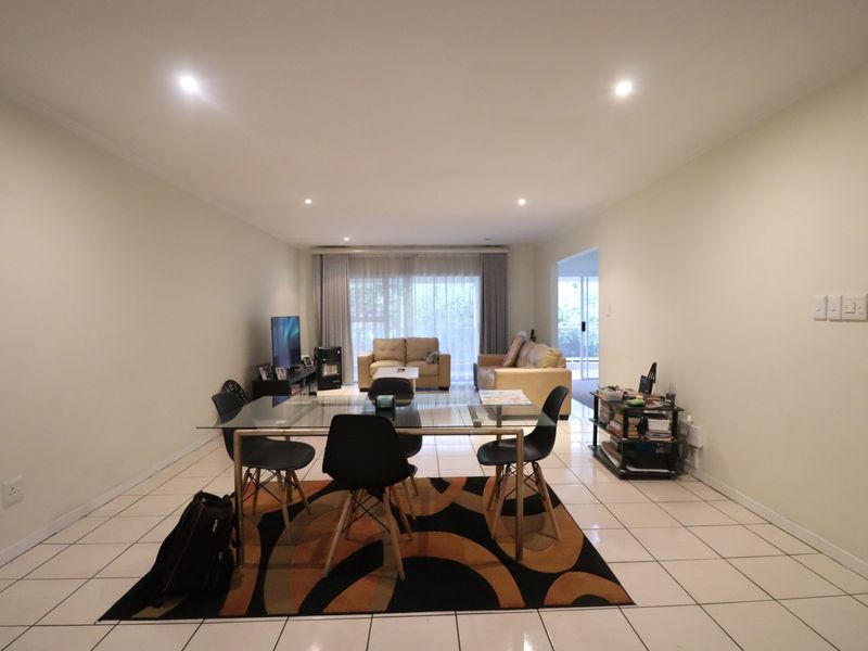 Spacious open-plan living and dining area featuring neutral tiled flooring, recessed downlighting, and a sliding glass door leading to an outdoor space.