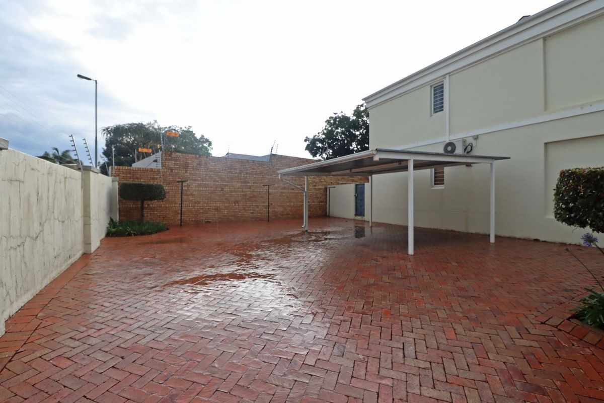 A paved rear courtyard area featuring a covered carport, perimeter boundary walls with electric fencing, and an external air conditioning unit.