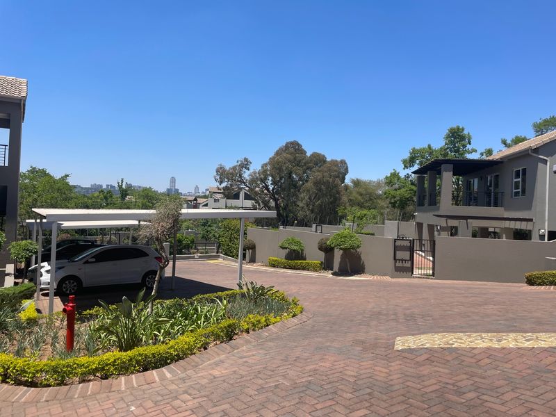 A well-maintained exterior view of the apartment complex featuring a paved driveway, covered parking bays, and secure perimeter walling.