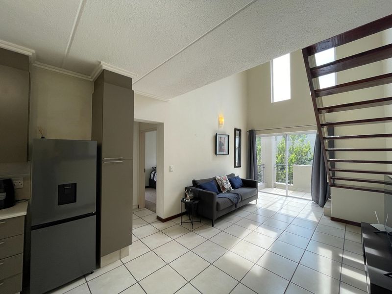 Open-plan living area featuring tiled floors, a double-volume ceiling, and a staircase leading to the upper level, with direct access to a balcony.