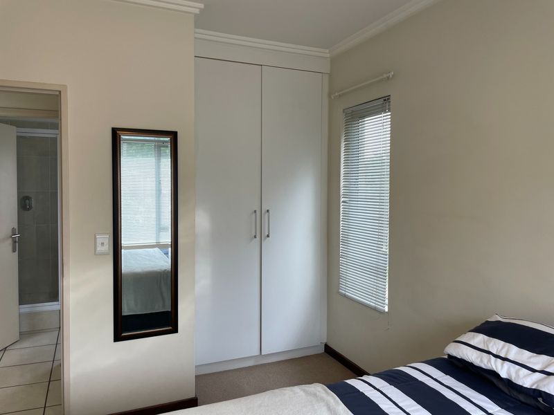 A well-maintained bedroom featuring built-in wardrobes, neutral wall finishes, carpeted flooring, and venetian blinds, with an adjacent bathroom visible through the doorway.