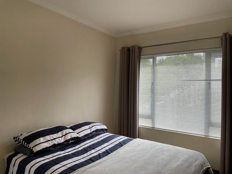 A well-maintained bedroom featuring neutral wall tones, a large window with fitted venetian blinds, and decorative ceiling coving.