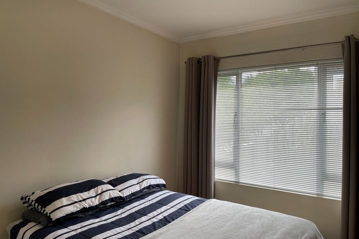 A well-maintained bedroom featuring neutral wall tones, a large window with fitted venetian blinds, and decorative ceiling coving.