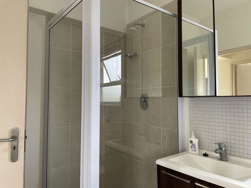 A functional bathroom featuring a glass-enclosed shower, a vanity unit with a basin, and a mirrored medicine cabinet with neutral wall tiling.