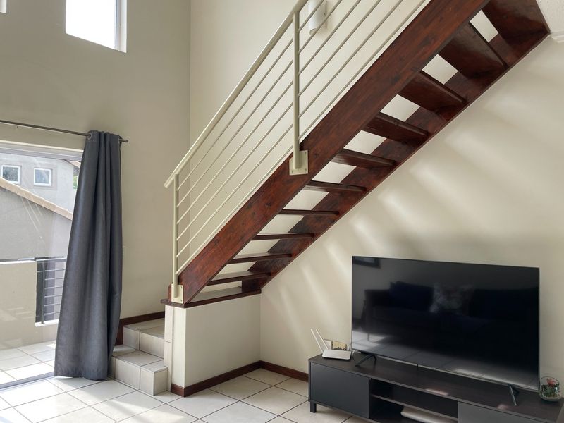 Living area featuring a prominent wooden staircase with metal balustrade, tiled flooring, and access to an outdoor balcony through a sliding glass door.